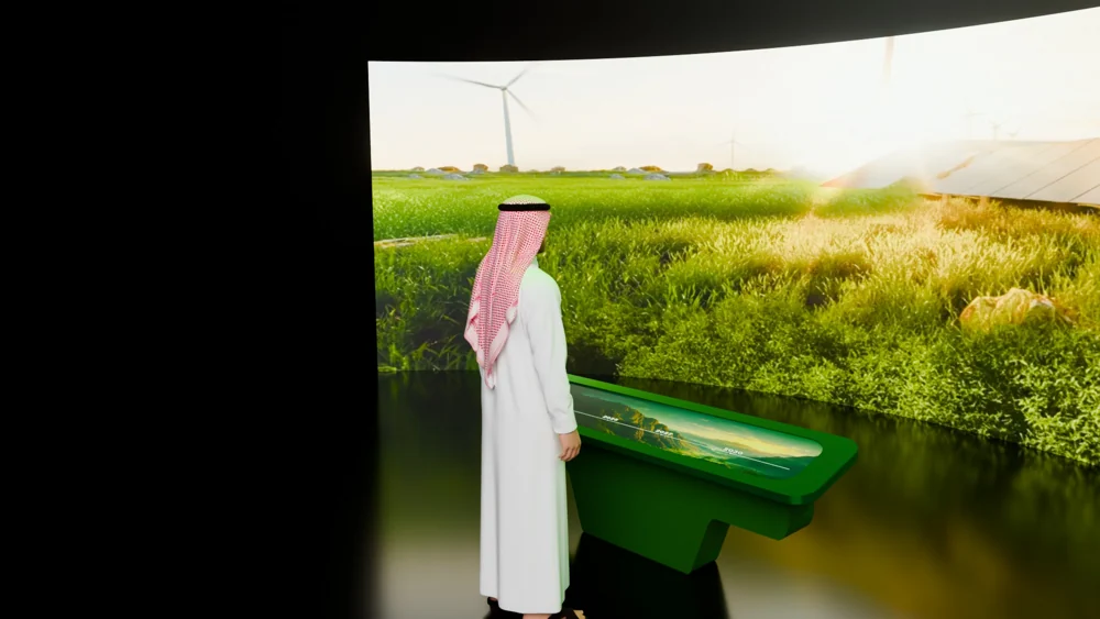 Curved landscape screen behind a long green interaction table and a scale figure.